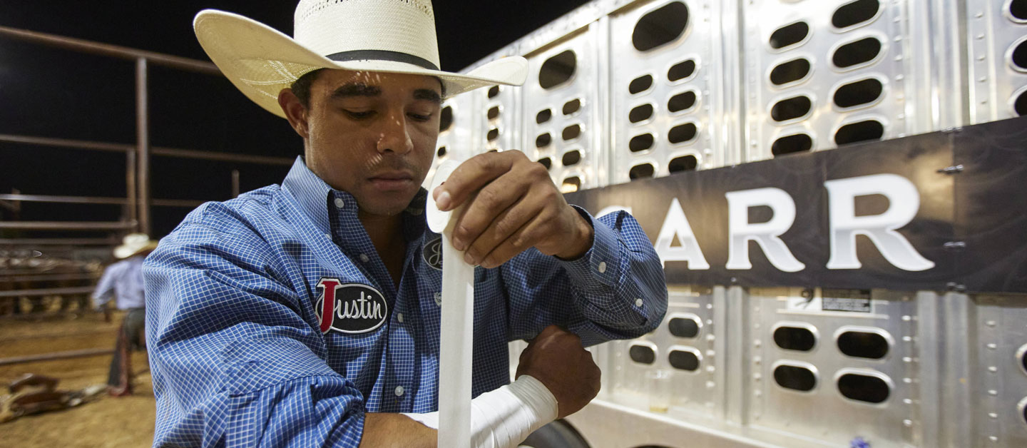 Laramie Mosley wearing a blue shirt taping up his wrist, preparing for the rodeo.